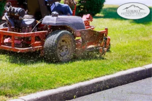 Professional lawn mowing with a red riding mower along a curb in Lethbridge, showcasing expert landscaping and property maintenance services.